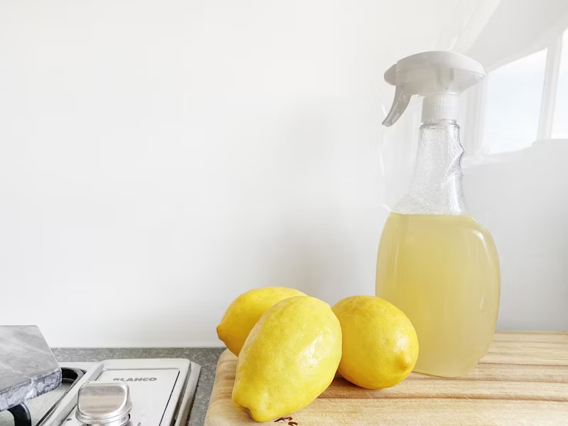 A clear spray bottle of pale natural cleaner beside fresh lemons on a kitchen counter