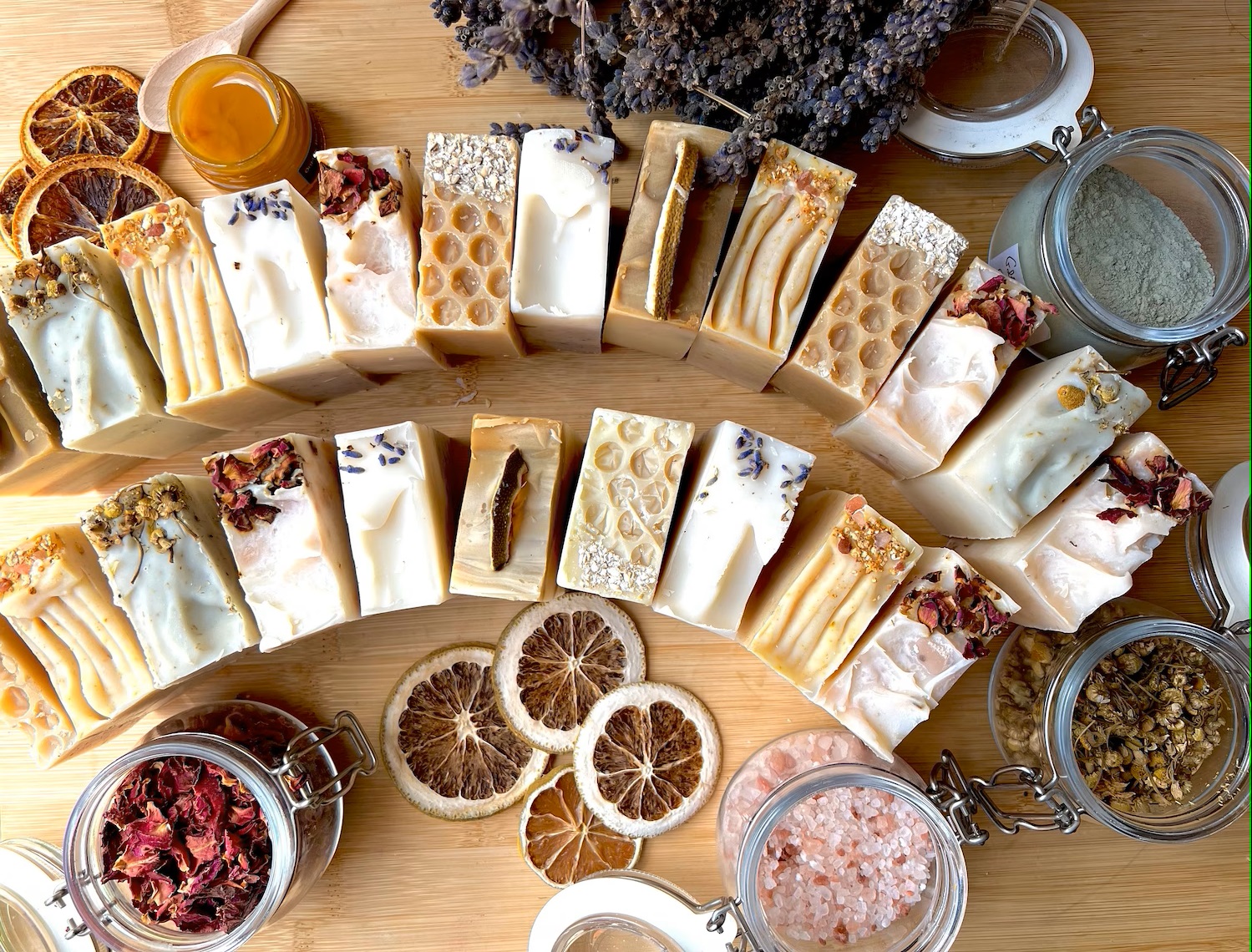 Rows of handmade artisan soap bars with lavender, dried citrus, honey, and botanicals on a wooden table