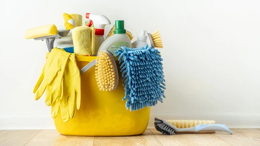 A yellow bucket holding sponges, brushes, gloves, and spray bottles, ready for a deep clean